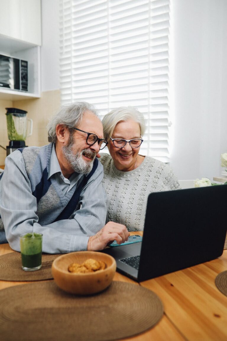 An elderly couple using a laptop in the kitchen.